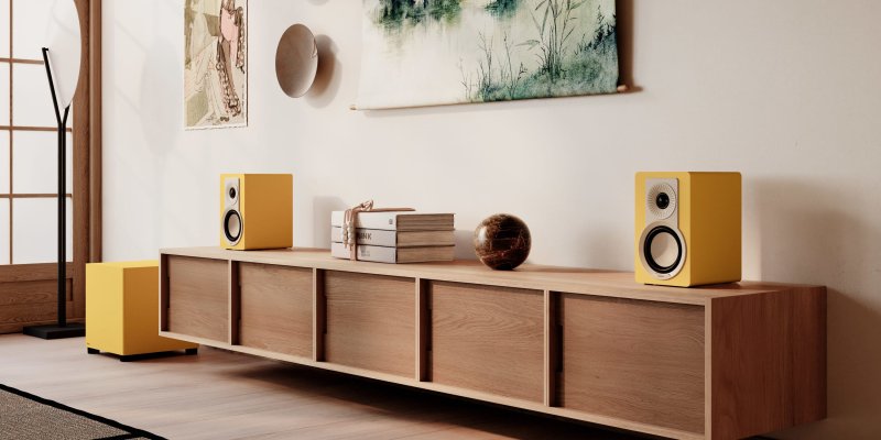 DALI BASIK SUB in Golden Yellow beside a low sideboard with a pair of matching standmount speakers
