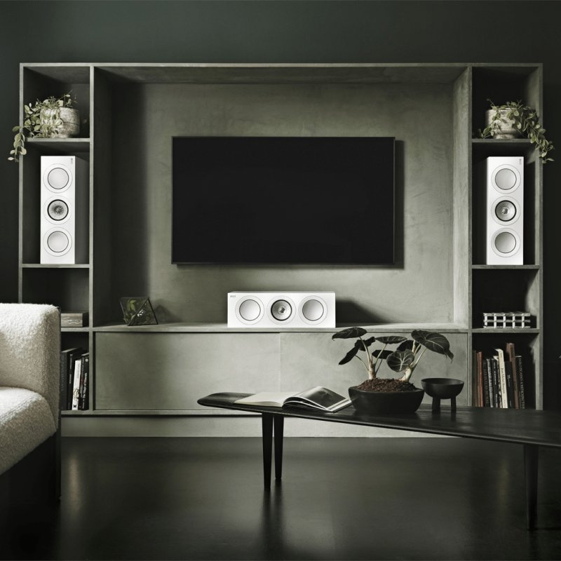 KEF R6 Meta Centre Speaker in a living room beneath a TV with R3 Meta standmounts, White Gloss finish shown