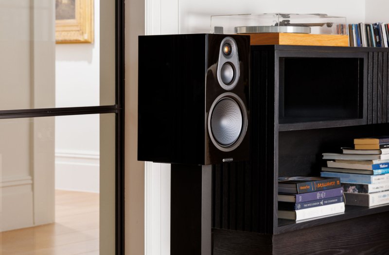 Monitor Audio Silver 100 8G High Gloss Black on a speaker stand in a living room setting
