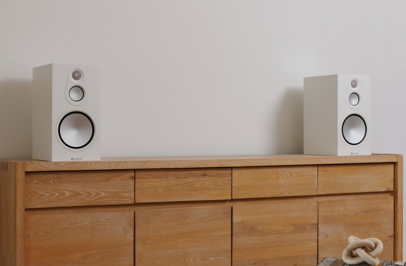 Monitor Audio Silver 100 8G Satin White on a wooden sideboard in a living room setting